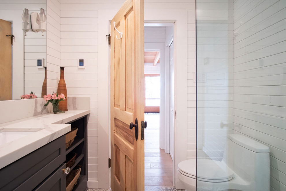 サンフランシスコにある高級な小さなトラディショナルスタイルのおしゃれなバスルーム (浴槽なし) (シェーカースタイル扉のキャビネット、青いキャビネット、一体型トイレ	、白いタイル、サブウェイタイル、白い壁、セメントタイルの床、オーバーカウンターシンク、珪岩の洗面台、グレーの床、開き戸のシャワー、白い洗面カウンター、シャワーベンチ、洗面台1つ、造り付け洗面台、板張り天井、パネル壁) の写真