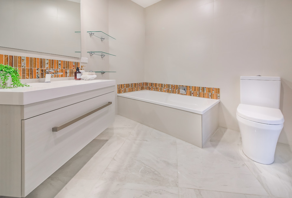 Стильный дизайн: ванная комната среднего размера в морском стиле с плоскими фасадами, белыми фасадами, угловой ванной, угловым душем, раздельным унитазом, оранжевой плиткой, плиткой мозаикой, белыми стенами, мраморным полом, монолитной раковиной, белым полом и душем с распашными дверями - последний тренд