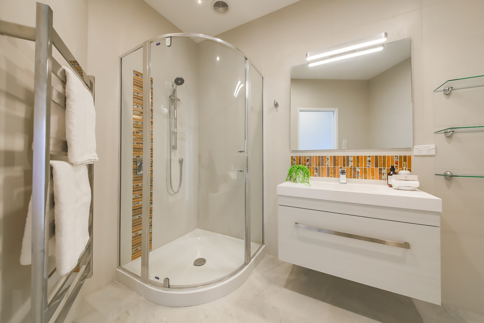 This is an example of a medium sized coastal bathroom in Wellington with flat-panel cabinets, white cabinets, a corner shower, orange tiles, mosaic tiles, marble flooring, an integrated sink, white floors, a hinged door and white walls.