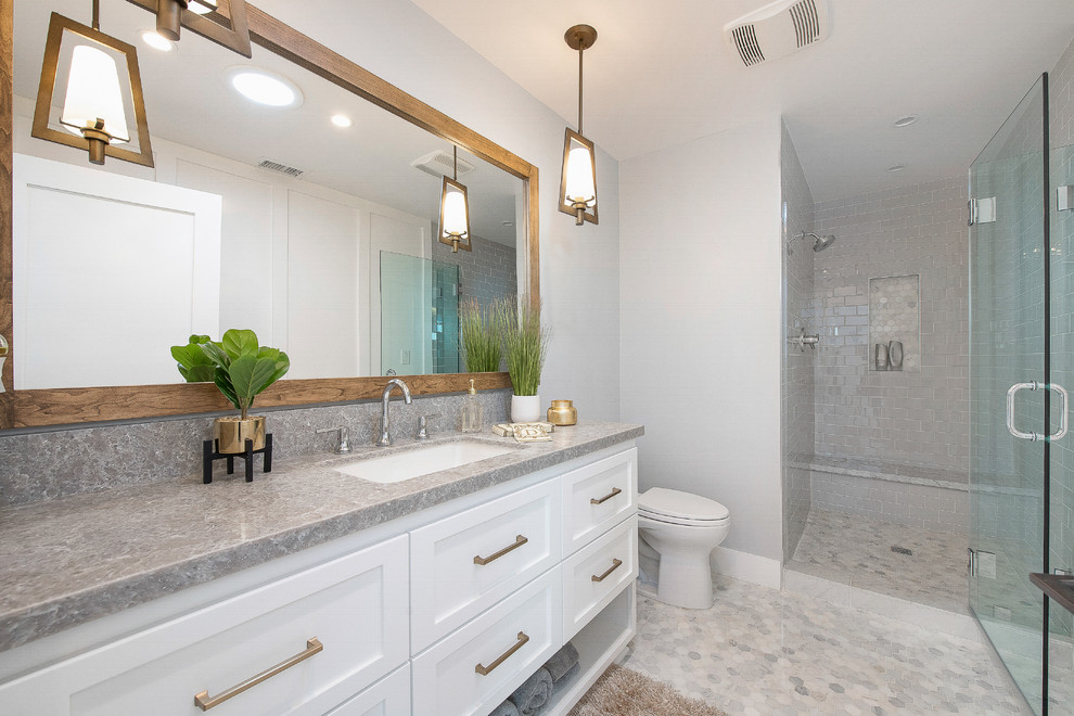 Example of a transitional master gray floor alcove shower design in Orange County with shaker cabinets, white cabinets, a two-piece toilet, white walls, an undermount sink, a hinged shower door and gray countertops