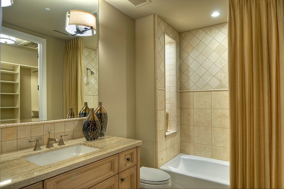 Immagine di una stanza da bagno minimal di medie dimensioni con lavabo sottopiano, ante in legno chiaro, vasca/doccia, WC monopezzo, piastrelle beige e pareti beige