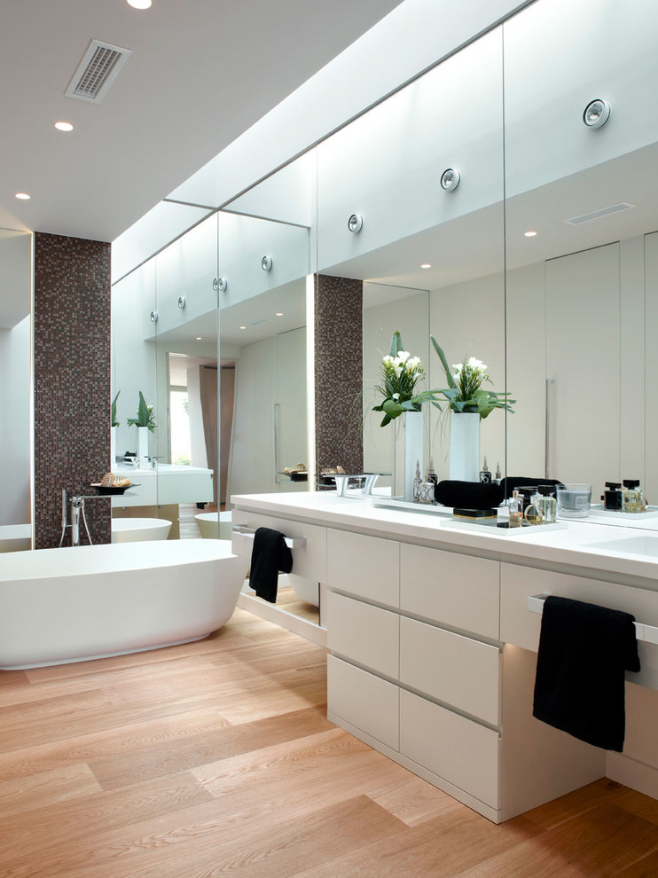 Cette image montre une salle de bain principale traditionnelle de taille moyenne avec un placard à porte plane, des portes de placard blanches, une baignoire indépendante, un combiné douche/baignoire, un sol en bois brun et un lavabo intégré.