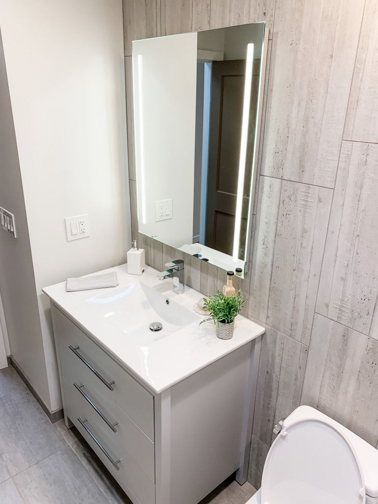 Idéer för att renovera ett litet funkis vit vitt badrum, med släta luckor, grå skåp, ett badkar i en alkov, en dusch/badkar-kombination, en toalettstol med hel cisternkåpa, grå kakel, porslinskakel, grå väggar, klinkergolv i porslin, ett integrerad handfat, bänkskiva i akrylsten, grått golv och dusch med duschdraperi