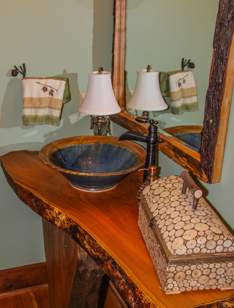 Cette image montre une grande salle de bain chalet en bois brun avec un placard en trompe-l'oeil, un plan de toilette en bois, un mur vert et un sol en bois brun.