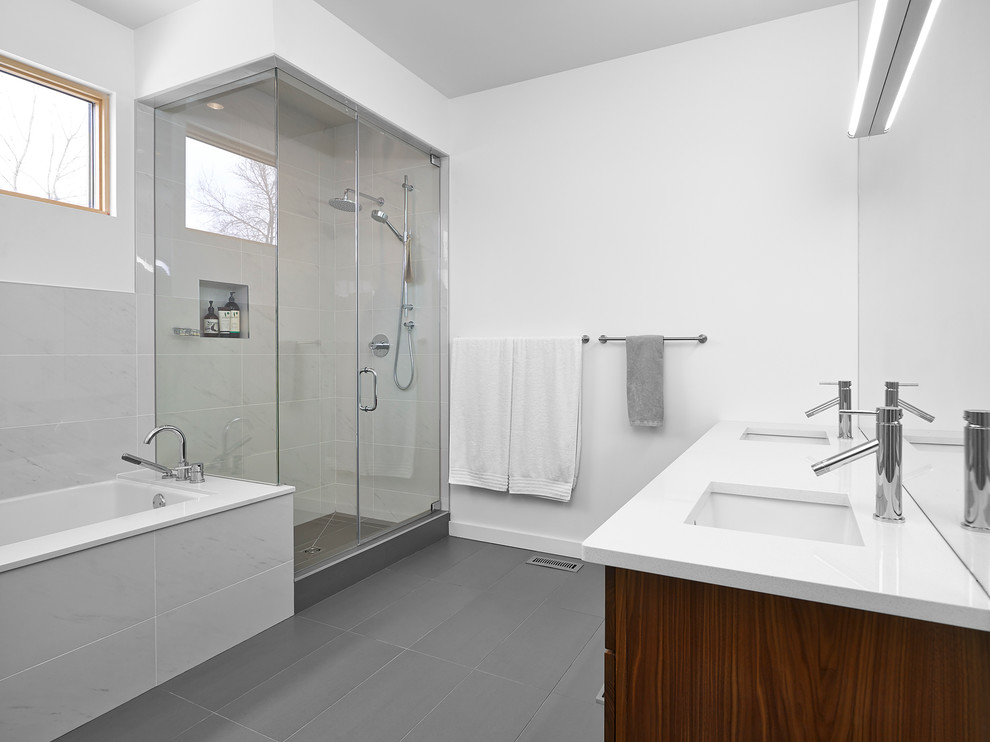 Cette image montre une salle de bain principale et grise et blanche minimaliste en bois brun de taille moyenne avec un lavabo encastré, un sol gris, un placard à porte plane, une baignoire encastrée, une douche d'angle, un carrelage gris, un carrelage de pierre, un mur blanc, sol en stratifié, un plan de toilette en quartz modifié et une cabine de douche à porte battante.