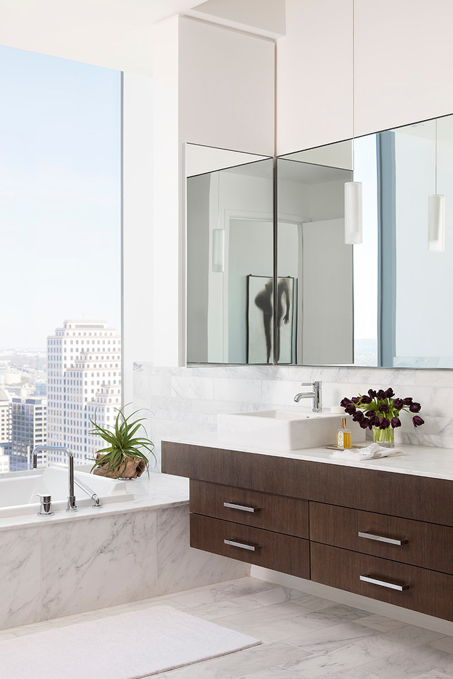 Foto de cuarto de baño principal actual con armarios con paneles lisos, puertas de armario de madera en tonos medios, bañera encastrada, baldosas y/o azulejos blancos, paredes blancas, lavabo sobreencimera, suelo blanco, encimeras blancas y espejo con luz