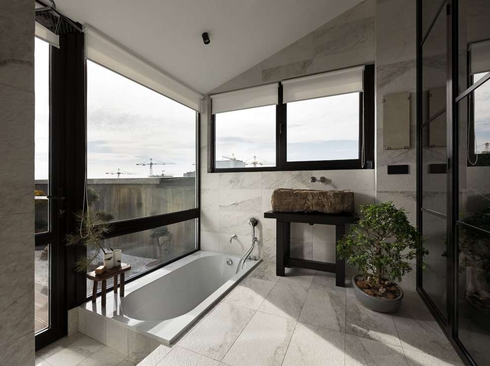 Modelo de cuarto de baño principal de estilo zen con bañera encastrada, baldosas y/o azulejos grises, lavabo sobreencimera, suelo gris y encimeras negras