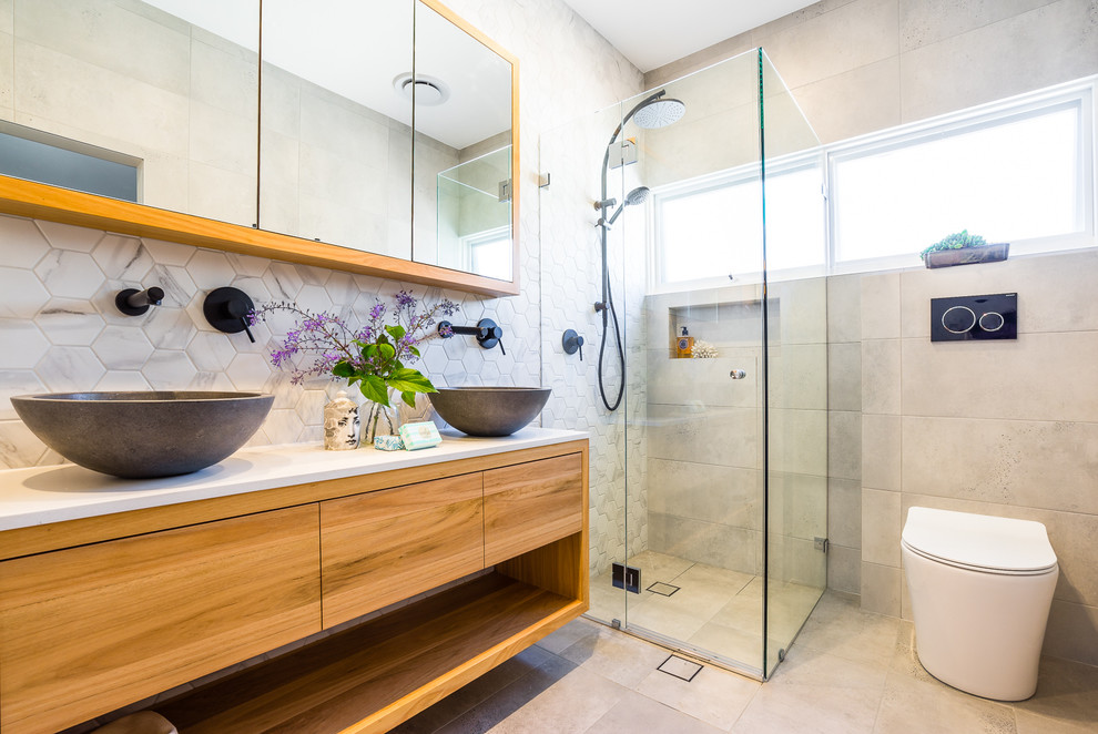 Aménagement d'une salle d'eau contemporaine en bois brun avec un placard à porte plane, une douche d'angle, WC à poser, un carrelage gris, un mur gris, une vasque, un sol gris, une cabine de douche à porte battante et un plan de toilette blanc.