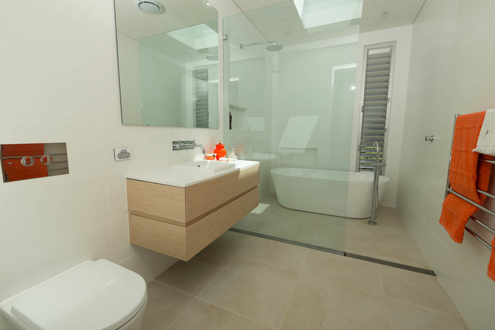 Inspiration pour une salle de bain design en bois clair avec un placard à porte plane, une baignoire indépendante, un espace douche bain, WC à poser, un carrelage blanc et un mur blanc.