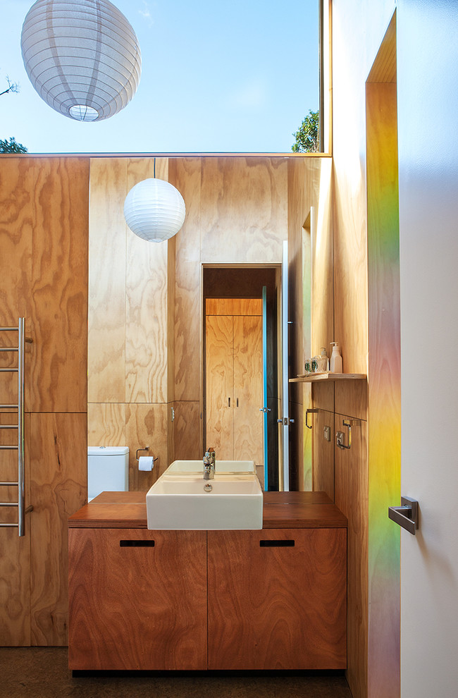 Foto de cuarto de baño contemporáneo con lavabo sobreencimera, armarios con paneles lisos, puertas de armario de madera oscura y encimera de madera