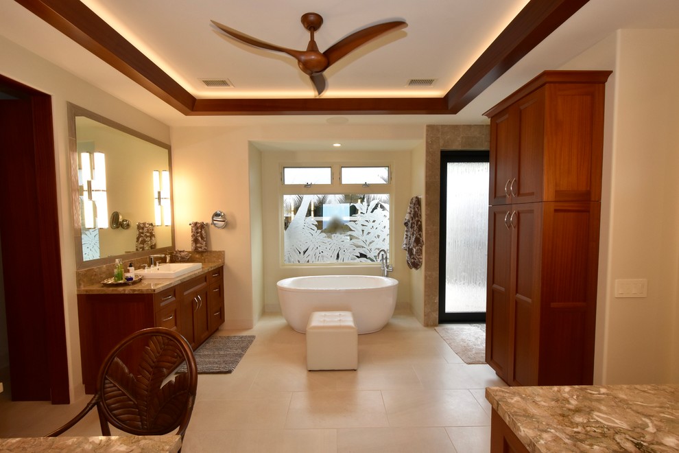 Large island style master beige tile and stone tile travertine floor bathroom photo in Hawaii with recessed-panel cabinets, dark wood cabinets, a one-piece toilet, beige walls, a drop-in sink and granite countertops