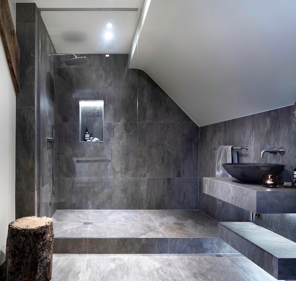 Modern inredning av ett litet grå grått badrum med dusch, med öppna hyllor, våtrum, en vägghängd toalettstol, grå kakel, porslinskakel, grå väggar, klinkergolv i porslin, ett avlångt handfat, kaklad bänkskiva, grått golv och med dusch som är öppen