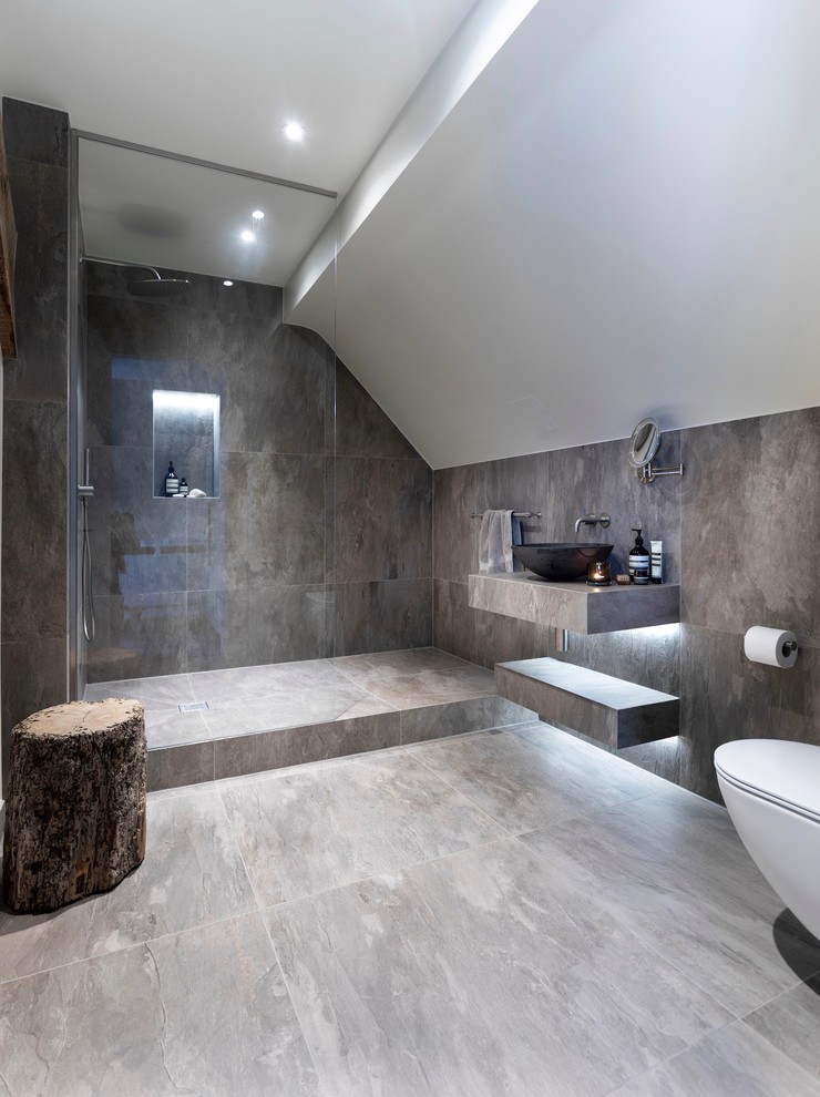 Inredning av ett modernt litet grå grått badrum med dusch, med öppna hyllor, våtrum, en vägghängd toalettstol, grå kakel, porslinskakel, grå väggar, klinkergolv i porslin, ett avlångt handfat, kaklad bänkskiva, grått golv och med dusch som är öppen