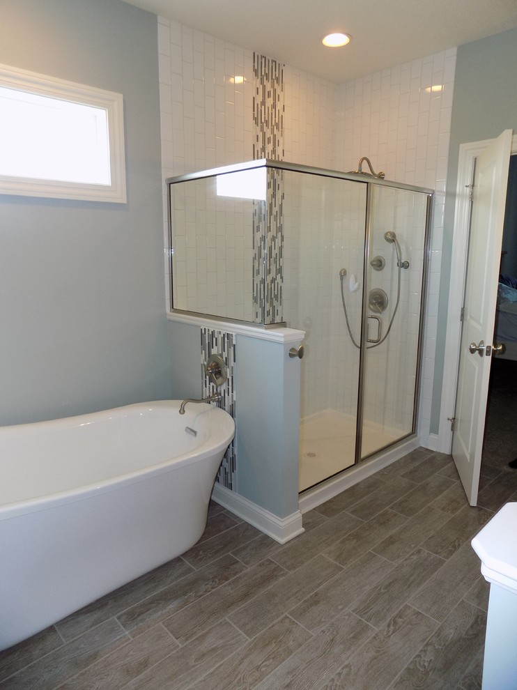 Photo of a medium sized traditional ensuite bathroom in Columbus with recessed-panel cabinets, grey cabinets, a freestanding bath, an alcove shower, a two-piece toilet, white tiles, ceramic tiles, blue walls, cement flooring, a submerged sink, granite worktops, brown floors and a hinged door.