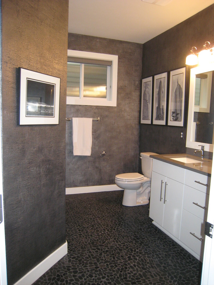 Inredning av ett modernt en-suite badrum, med ett undermonterad handfat, släta luckor, vita skåp, bänkskiva i kvarts, ett badkar i en alkov, en dusch i en alkov, en toalettstol med separat cisternkåpa, svart kakel, kakel i småsten, svarta väggar och klinkergolv i småsten