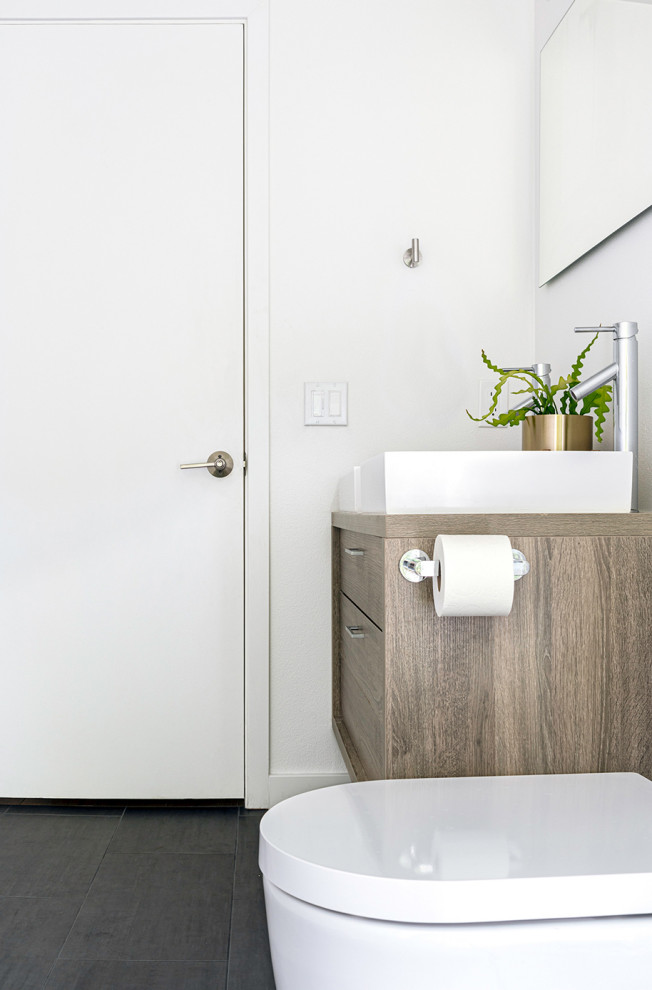 Стильный дизайн: главная ванная комната среднего размера в стиле модернизм с плоскими фасадами, светлыми деревянными фасадами, душем без бортиков, унитазом-моноблоком, белой плиткой, керамогранитной плиткой, белыми стенами, полом из керамогранита, настольной раковиной, столешницей из дерева, черным полом, открытым душем и белой столешницей - последний тренд