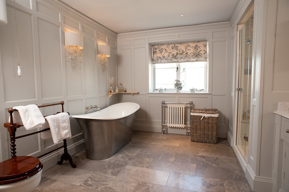 Inredning av ett klassiskt mellanstort badrum, med ett fristående badkar, en toalettstol med separat cisternkåpa, stenkakel och grå väggar