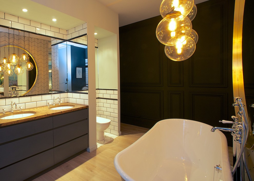Modern inredning av ett mellanstort en-suite badrum, med släta luckor, grå skåp, ett fristående badkar, vit kakel, tunnelbanekakel, svarta väggar, ljust trägolv, ett undermonterad handfat och träbänkskiva