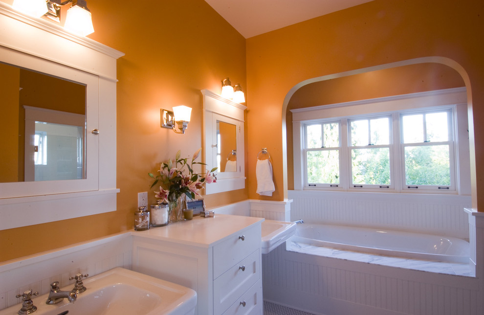 シアトルにある中くらいなトラディショナルスタイルのおしゃれなマスターバスルーム (ペデスタルシンク、白いキャビネット、アルコーブ型浴槽、オレンジの壁) の写真
