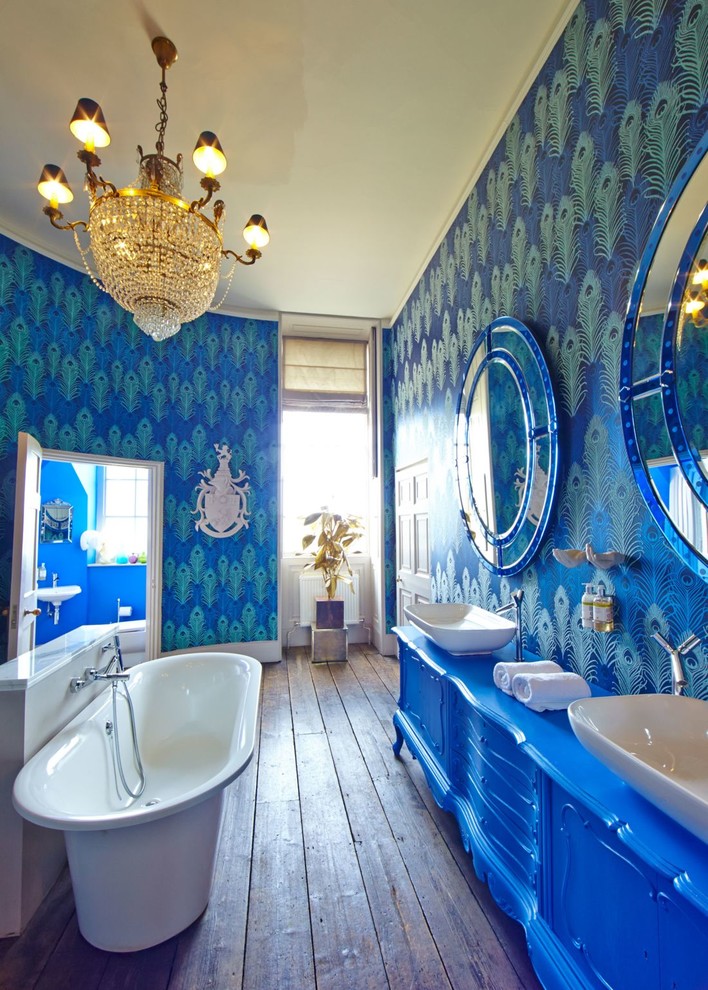 Imagen de cuarto de baño infantil bohemio grande con puertas de armario azules, bañera exenta, combinación de ducha y bañera, paredes azules, suelo de madera oscura, lavabo sobreencimera y armarios con paneles empotrados