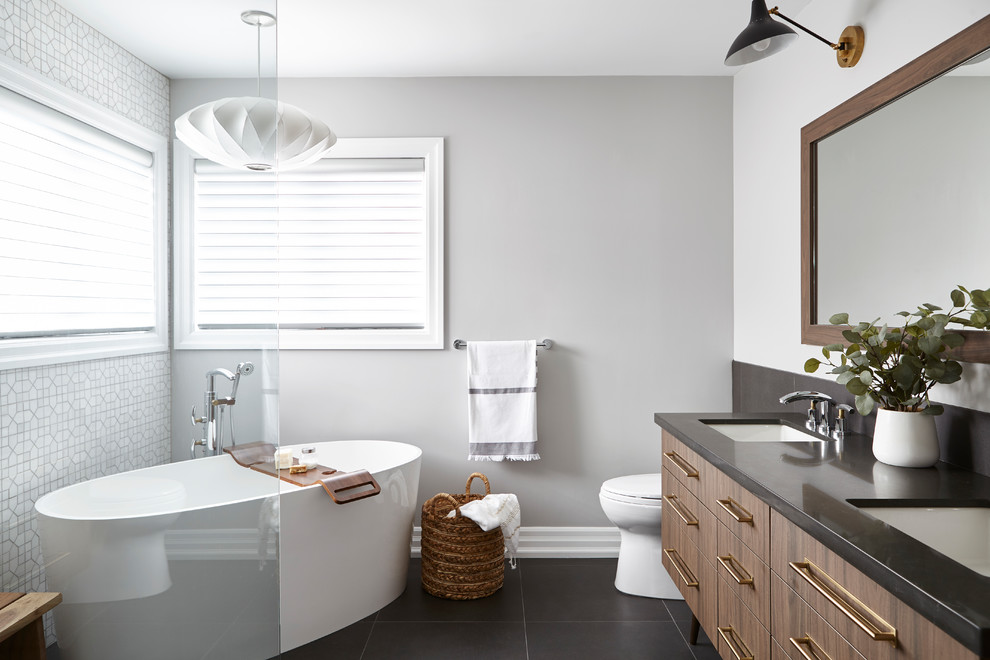 Пример оригинального дизайна: ванная комната в современном стиле с плоскими фасадами, фасадами цвета дерева среднего тона, отдельно стоящей ванной, белой плиткой, серыми стенами, врезной раковиной, черным полом и черной столешницей