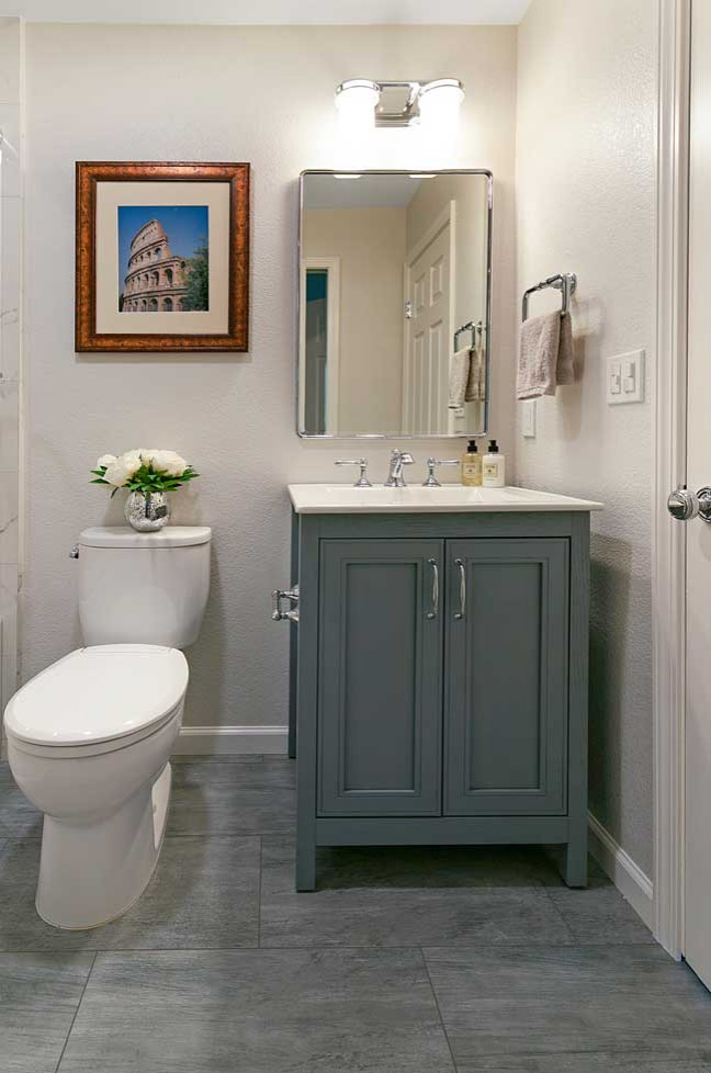 На фото: маленькая ванная комната в стиле неоклассика (современная классика) с фасадами с утопленной филенкой, синими фасадами, ванной в нише, душем над ванной, раздельным унитазом, белой плиткой, керамогранитной плиткой, бежевыми стенами, полом из керамогранита, монолитной раковиной, серым полом, душем с раздвижными дверями, белой столешницей, тумбой под одну раковину и напольной тумбой для на участке и в саду