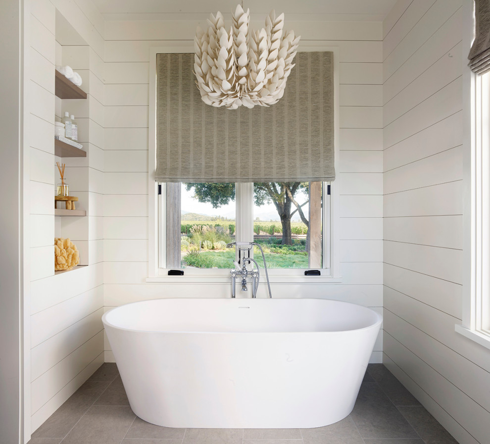 Example of a farmhouse gray floor and shiplap wall freestanding bathtub design in San Francisco with white walls and a niche