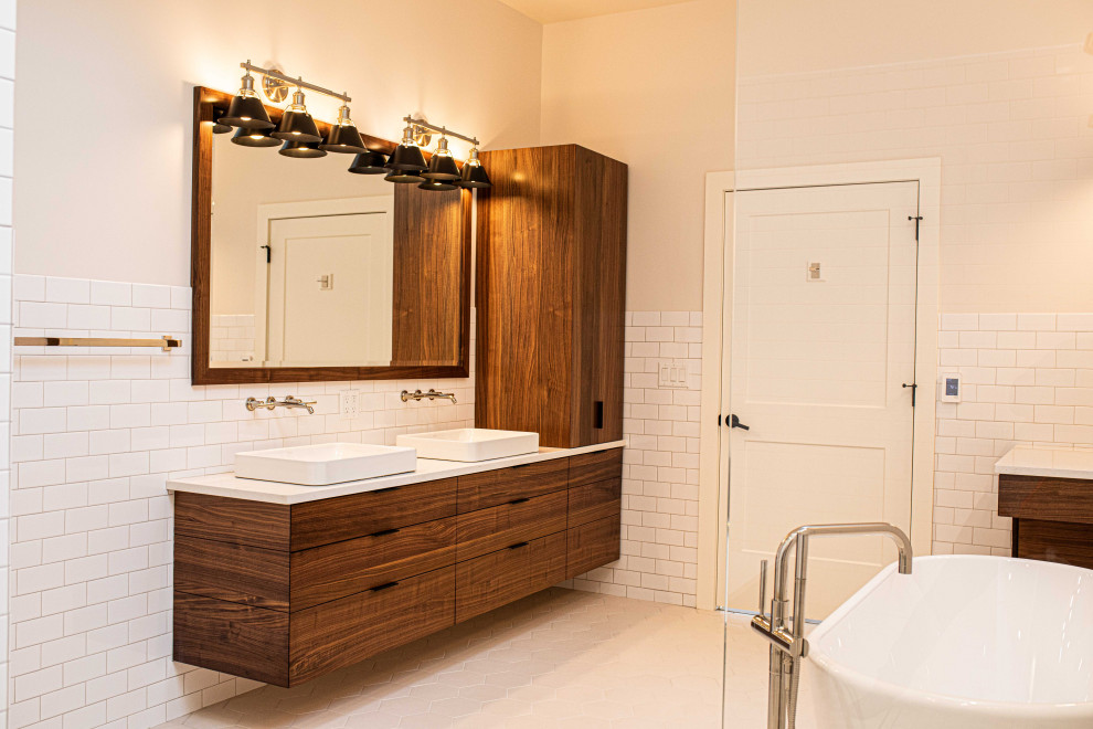 Пример оригинального дизайна: большая главная ванная комната в современном стиле с плоскими фасадами, коричневыми фасадами, отдельно стоящей ванной, душевой комнатой, унитазом-моноблоком, белой плиткой, керамической плиткой, разноцветными стенами, полом из керамогранита, настольной раковиной, столешницей из искусственного кварца, белым полом, открытым душем, белой столешницей, сиденьем для душа, тумбой под две раковины, подвесной тумбой и сводчатым потолком