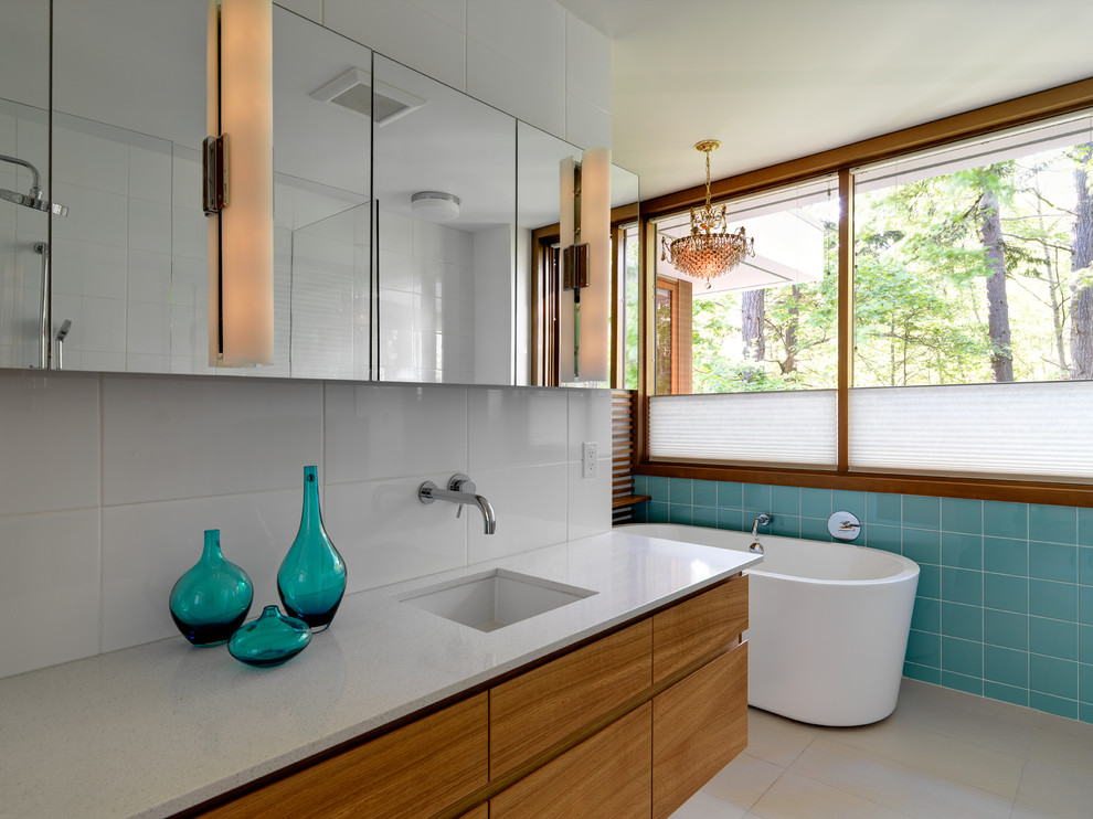 Diseño de cuarto de baño de nogal moderno con armarios con paneles lisos, puertas de armario de madera oscura, bañera exenta y baldosas y/o azulejos azules