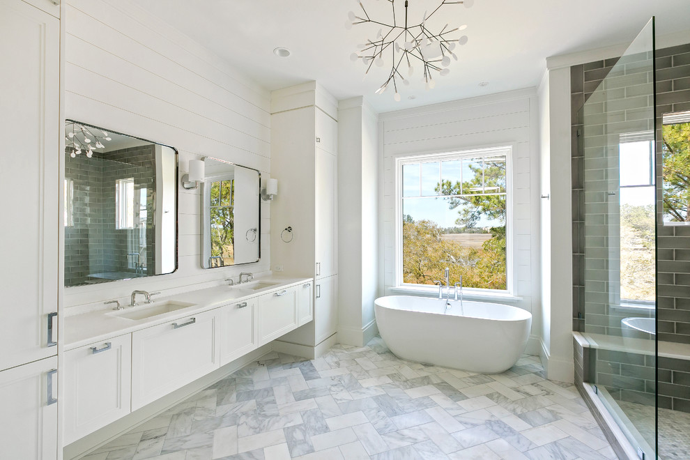 Foto de cuarto de baño clásico renovado con armarios estilo shaker, puertas de armario blancas, bañera exenta, baldosas y/o azulejos blancos, paredes blancas, lavabo bajoencimera y suelo gris