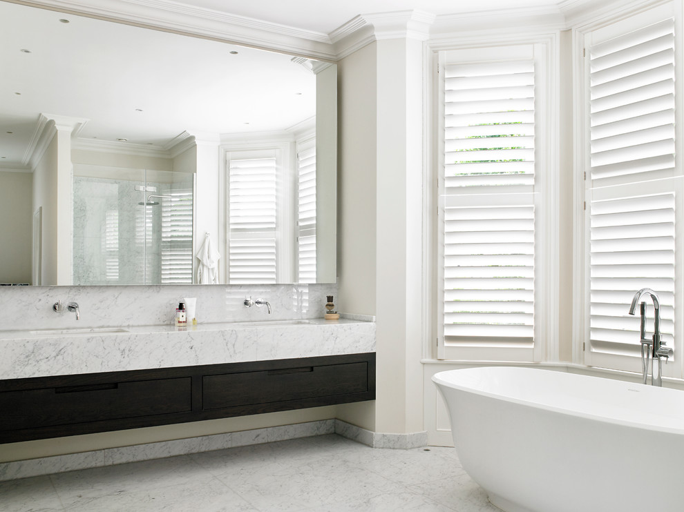 Modelo de cuarto de baño principal clásico renovado con armarios con paneles lisos, puertas de armario de madera en tonos medios, bañera exenta y paredes beige