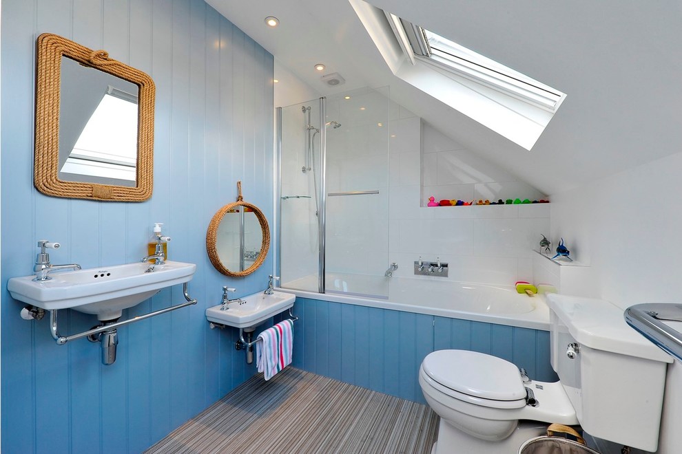 Foto på ett maritimt badrum, med ett väggmonterat handfat, ett badkar i en alkov, en dusch/badkar-kombination, en toalettstol med separat cisternkåpa, vit kakel och blå väggar