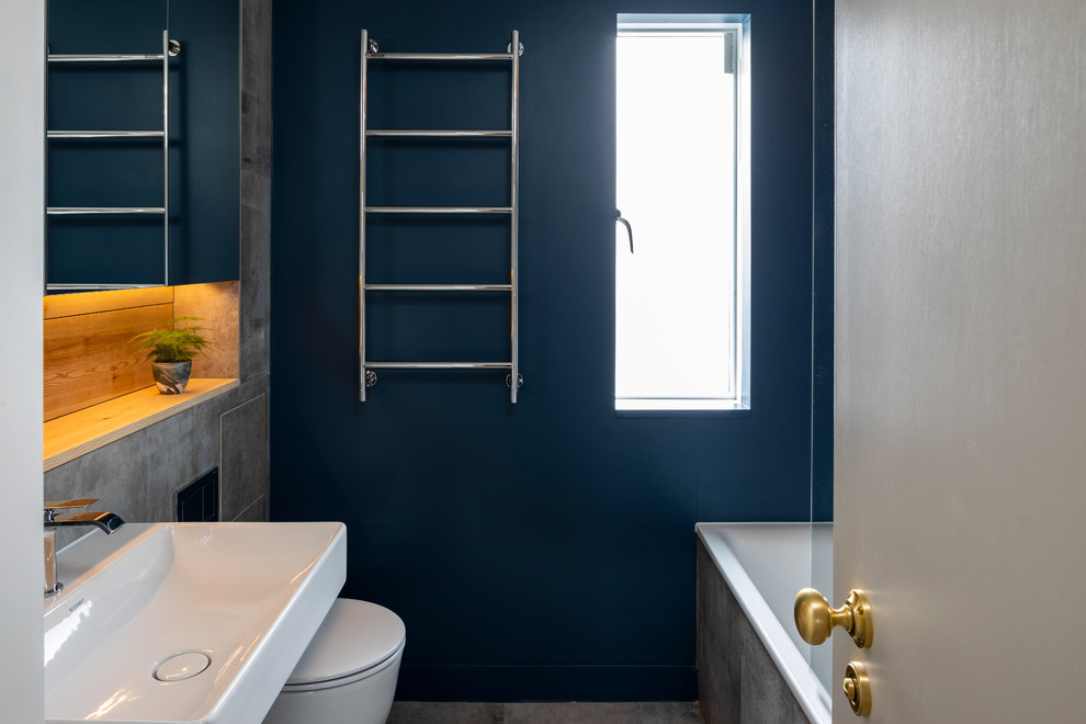 Foto på ett litet funkis grå en-suite badrum, med öppna hyllor, skåp i ljust trä, en öppen dusch, en toalettstol med hel cisternkåpa, blå kakel, stenkakel, blå väggar, cementgolv, ett väggmonterat handfat, bänkskiva i betong, grått golv och med dusch som är öppen