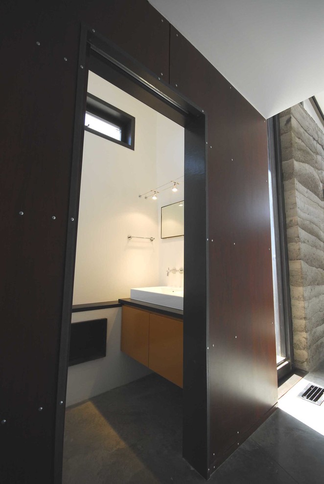 Foto di una piccola stanza da bagno con doccia moderna con ante lisce, ante in legno scuro, pareti marroni, pavimento in cemento, lavabo a bacinella e top in superficie solida