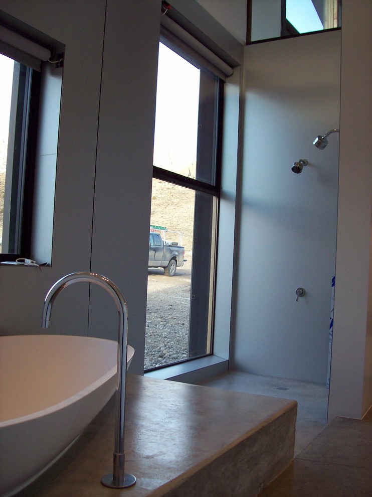 Cette image montre une petite salle de bain principale minimaliste avec un placard à porte plane, une douche ouverte, un mur gris, sol en béton ciré, une vasque et un plan de toilette en surface solide.