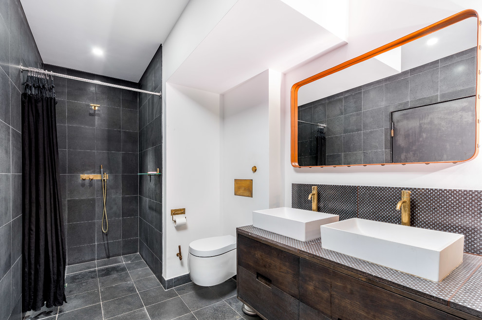 Cette image montre une salle de bain urbaine en bois foncé avec un placard à porte plane, un plan de toilette en carrelage, une douche à l'italienne, WC suspendus, un carrelage gris, un mur blanc, une vasque, un sol gris et une cabine de douche avec un rideau.