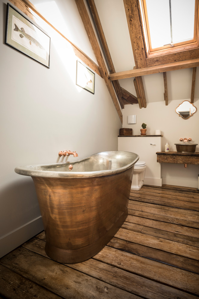 Inspiration for a country ensuite bathroom in Hampshire with medium wood cabinets, a freestanding bath, white walls, dark hardwood flooring, a vessel sink, wooden worktops, brown floors and brown worktops.