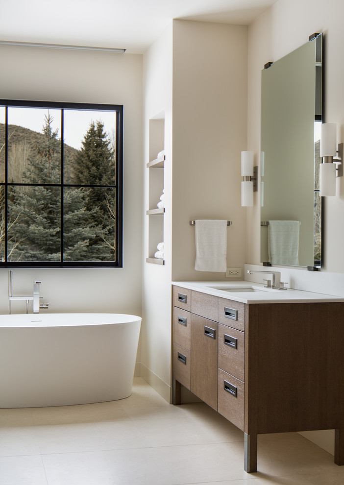 Foto de cuarto de baño principal actual con puertas de armario de madera en tonos medios, bañera exenta, paredes beige y armarios con paneles lisos