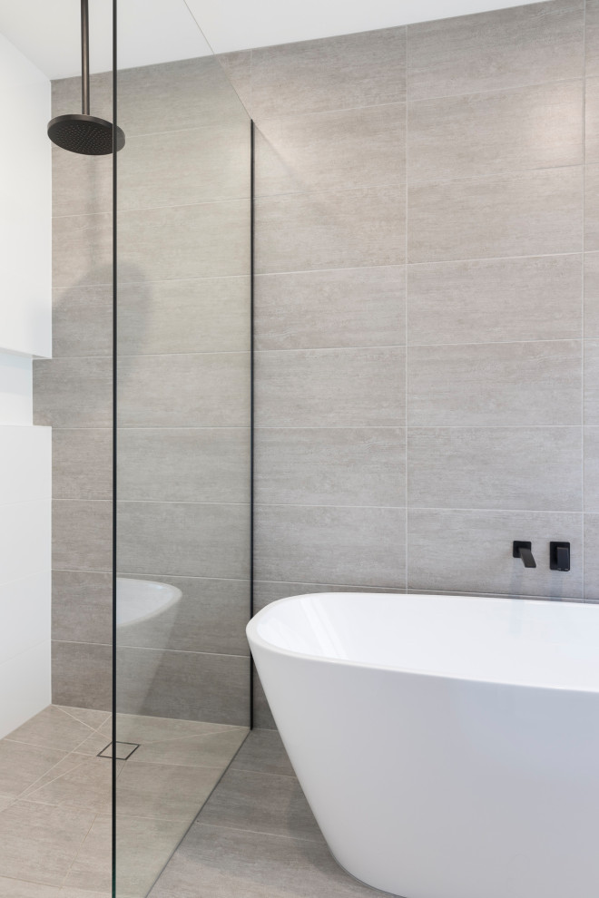 На фото: главная ванная комната среднего размера в современном стиле с отдельно стоящей ванной, открытым душем, серой плиткой, керамической плиткой, серыми стенами, полом из керамической плитки, серым полом и открытым душем с