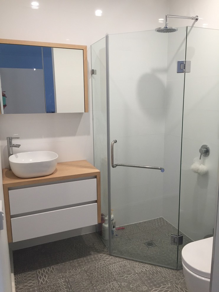Exemple d'une petite salle d'eau tendance avec un placard à porte plane, des portes de placard blanches, une douche d'angle, un mur blanc, sol en béton ciré, une vasque et un carrelage blanc.