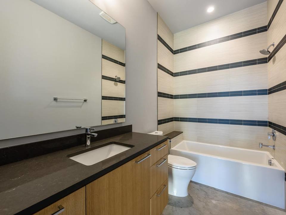 Cette image montre une salle de bain design en bois brun de taille moyenne pour enfant avec un placard à porte plane, une baignoire en alcôve, un combiné douche/baignoire, WC à poser, un carrelage noir et blanc, des carreaux de porcelaine, un mur gris, sol en béton ciré, un lavabo encastré et un plan de toilette en quartz modifié.