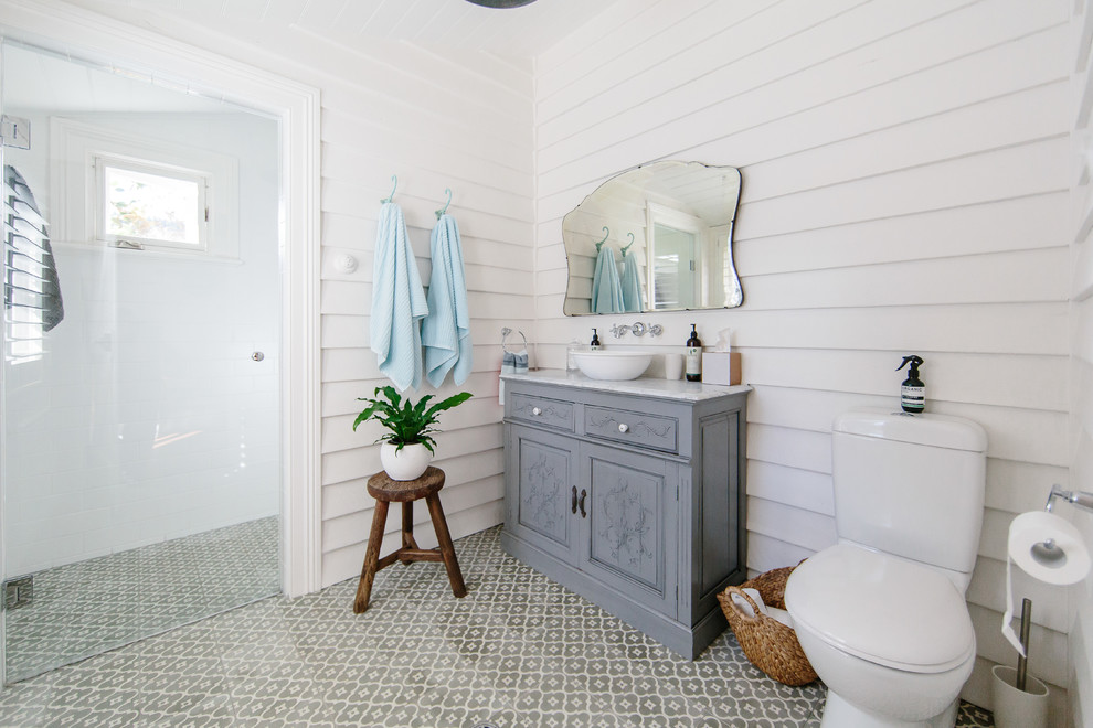 Foto på ett shabby chic-inspirerat grå badrum med dusch, med grå skåp, en kantlös dusch, en toalettstol med separat cisternkåpa, vita väggar, ett fristående handfat, flerfärgat golv, dusch med gångjärnsdörr och luckor med upphöjd panel