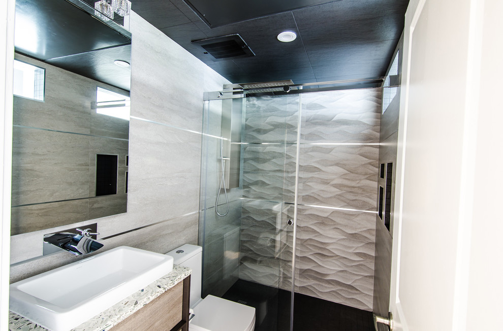 Пример оригинального дизайна: главная ванная комната среднего размера в современном стиле с настольной раковиной, плоскими фасадами, серыми фасадами, столешницей из переработанного стекла, душем в нише, унитазом-моноблоком, серой плиткой, керамогранитной плиткой, серыми стенами и полом из керамогранита