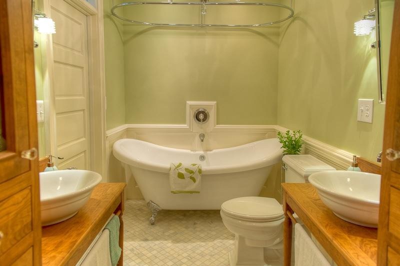 Inredning av ett klassiskt litet en-suite badrum, med ett fristående handfat, möbel-liknande, skåp i ljust trä, träbänkskiva, ett badkar med tassar, en dusch/badkar-kombination, en toalettstol med separat cisternkåpa, grå kakel, mosaik, gröna väggar och marmorgolv
