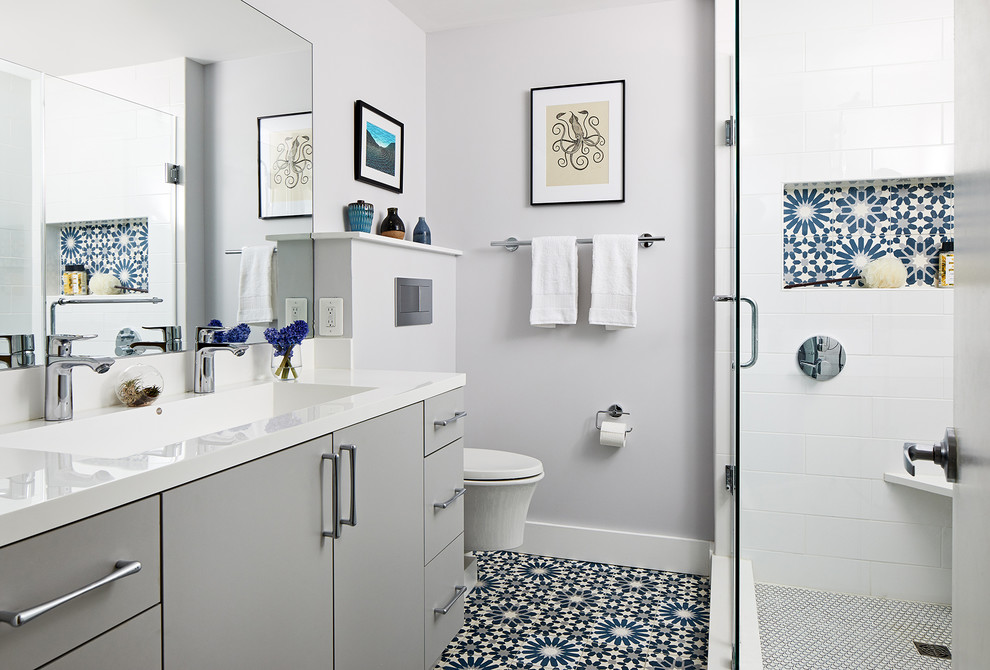 Modern inredning av ett mellanstort vit vitt badrum med dusch, med släta luckor, grå skåp, en hörndusch, en vägghängd toalettstol, vit kakel, grå väggar, dusch med gångjärnsdörr, ett integrerad handfat och blått golv