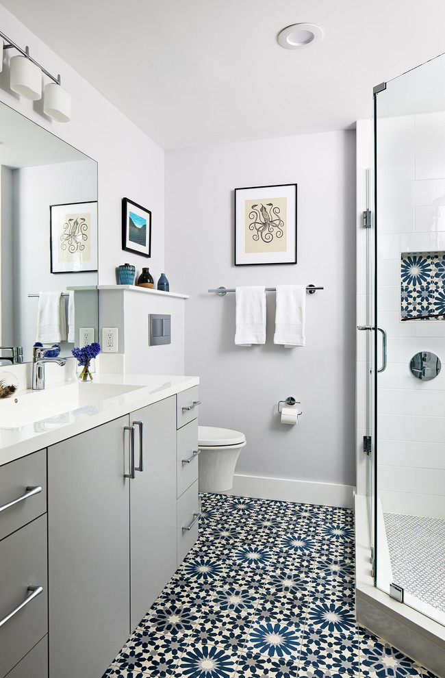 This is an example of a medium sized contemporary ensuite bathroom in DC Metro with flat-panel cabinets, grey cabinets, a corner shower, a wall mounted toilet, white tiles, grey walls, a hinged door and white worktops.