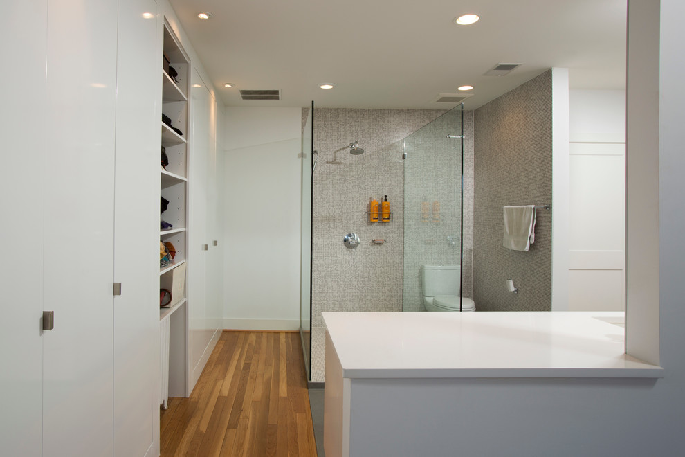 Inspiration for a large contemporary ensuite bathroom in DC Metro with a submerged sink, a walk-in shower, white walls, flat-panel cabinets, white cabinets, a two-piece toilet, grey tiles, mosaic tiles, solid surface worktops and light hardwood flooring.