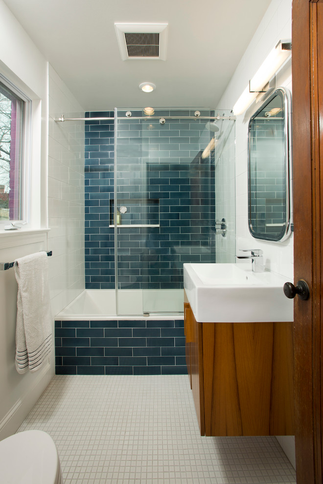На фото: детская ванная комната среднего размера в стиле фьюжн с плоскими фасадами, фасадами цвета дерева среднего тона, ванной в нише, душем над ванной, унитазом-моноблоком, синей плиткой, керамической плиткой, белыми стенами, настольной раковиной и полом из мозаичной плитки с