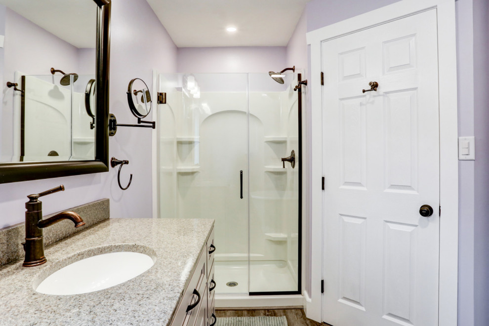 Foto på ett mellanstort amerikanskt beige en-suite badrum, med beige skåp, ett fristående badkar, en dusch i en alkov, lila väggar, vinylgolv, ett undermonterad handfat, marmorbänkskiva, brunt golv och dusch med gångjärnsdörr
