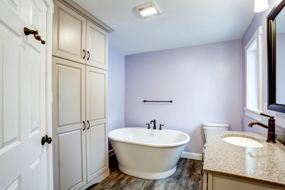 Foto på ett mellanstort amerikanskt beige en-suite badrum, med beige skåp, ett fristående badkar, en dusch i en alkov, lila väggar, vinylgolv, ett undermonterad handfat, marmorbänkskiva, brunt golv och dusch med gångjärnsdörr